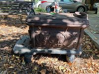 Left side view showing ornate design and 'Favorite Box' marking on the cast iron wood stove, with visible weathered and rusty patina on surface.