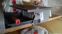 Full view of Workforce tile saw showing cutting table, water tray underneath, and blade guard with an orange handle.
