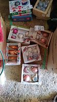 Photo showing five boxes of vintage Christmas ornaments including pink, copper, white textured, and multi-color star ornament set.