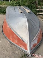 Upside-down view of boat hull showing red-painted sides and silver underside with two wooden oars on top.