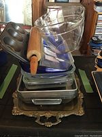 Stack of various glass and metal baking dishes with a wooden rolling pin on top, and the ornate silver plated serving tray at the base