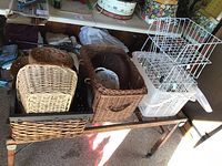 Photo showing wooden washtub stand with assortment of wicker baskets in natural brown and white plastic baskets on top, alongside white metal wire organizers.