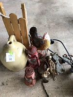 Photo shows a collection of various vintage items: large beige stoneware jug, two red metal hurricane lamps, metal rooster figurine, vintage strap-on metal roller skates, wooden sled, metal candle holder, and two metal grinders.
