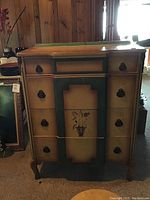 Front view of dresser showing painted floral design, drawer pulls, and wear on top surface.