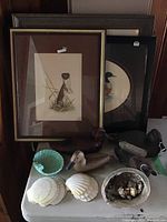 Table display showing framed prints, wooden ducks, ceramic dish and shells.