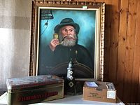 Lot overview showing painting on wall with metal lighthouse figurine, Fisherman's Friend tin box, and Tobacciana wooden box arranged below.