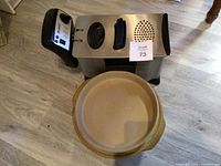 Bravetti deep fryer with control panel featuring dial, buttons, and indicator lights, placed on floor with Pampered Chef clay ware pieces next to it.