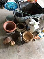 Wide view of gardening lot showing metal wash tub, clay pots, a decorative turtle figurine, glass flower stakes, and part of a watering can.