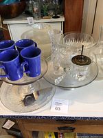 Multiple glass and ceramic items including blue ceramic mugs, glass bowls, cake stands, and utensils