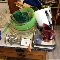 Overview of kitchenware including hand grinder, glass bowls with green rims, green glass tumblers, ceramic maroon and beige pitchers, wooden rolling pin, and metal blue dishes in background.