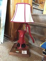 Full view of lamp showing red metal water pump with handle and fabric shade atop wood base.