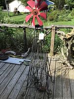 Metal windmill with red blades and metal trellis on wooden deck with garden background