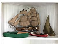 Overview of four model boats including Hurricane Clipper model ship, two painted wooden boats (green and red) and a brass metal sailboat
