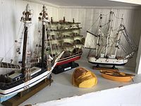 Shelf displaying three model ships, a small wooden rowboat, and a carved fisherman wall mount face.