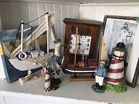 Photo of the entire nautical decor lot with wooden ships, figurines, clock, painting, and framed print arranged on white shelf.