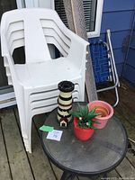 Four white plastic stackable patio chairs and a blue mesh lawn chair on deck outside a house, adjacent to a round glass table.