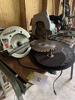 Two power circular saws on a work table along with saw blades and grinding discs.