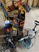Overview of the lot showing the rolling basket, hand saws, pump sprayer, and coiled cords placed on a concrete floor in a workshop setting.