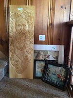 Photo showing the wood carved panel and grouped framed prints and paintings leaning against wood paneled wall by stairs.