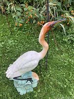 Photo of the bird statue on grass, showing detailed white body and rust-colored neck, standing on a blue-green base.