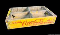 Front side of the wooden crate showing yellow paint and red Coca Cola branding text.