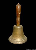 Front view of antique brass bell with wooden handle showing overall shape and patina.