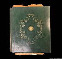 Front cover of the antique school workbook, dark green with gold design and initials