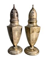 Front view of both antique sterling silver salt and pepper shakers showing hexagonal bodies and pointed finial tops with holes for dispensing.