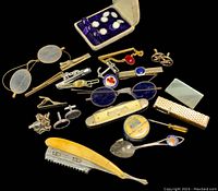 Collection of vintage cufflinks, assorted pins, a fork, and small tools on black background.