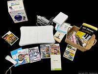 Lot items arranged including Balance Board, game discs, Wii remote, charging dock, balance ball box, books and manuals