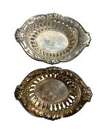 Top-down view of two oval sterling silver dishes with cutouts and ornate floral edges, showing decorative pattern and tarnish on one dish.