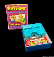 Original colorful Stori-viewer packaging with cartoon artwork and text. Inside the box is the teal plastic Stori-viewer toy and a packet of story slides labeled 'Stori-Views'.