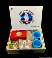 Photo showing White Owl Brand cigar box open with various items inside including a red box, blue Peking glass cups, and psychedelic fabric.