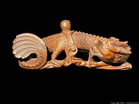 Side view of the hand carved wooden dragon showing detailed scales and curled tail with rounded knob on back.