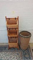 Front view of 3-tier woven storage cubby with wooden frame and tall woven laundry basket standing side by side on patterned rug against white brick wall.