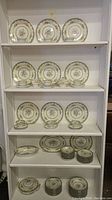 Full shelving display showing multiple stacks of plates, bowls, cups, saucers, and serving dishes.