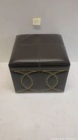Front view of black leather ottoman showing button tufting top and decorative nailhead trim