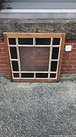 Full view of vintage stained glass window panel with wooden frame, showing overall appearance and size in outdoor setting.