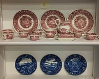 Full view of Mason's red transferware china cups, saucers, creamer, butter dish, and Wedgwood blue transferware cabinet plates showing all items in the lot.