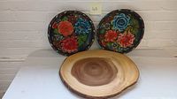 Three items: two hand-painted floral wall plates with colorful flowers on black background, and one circular wooden lazy Susan with natural wood grain and smooth finish.