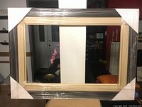 Full front view of large wood frame wrapped in plastic and corner protectors, showing overall size and finish.