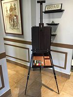 Front view of the portable wooden easel standing with open storage drawer containing gel markers and compartments