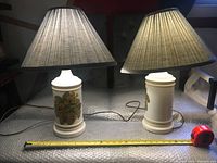 Two porcelain table lamps with floral designs and large conical fabric lampshades on a table with measurement tape showing height and diameter.