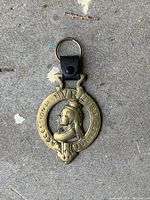 Image showing the brass horse medallion with a profile relief of Queen Victoria and embossed inscription, attached to a keyring with a black leather strap.