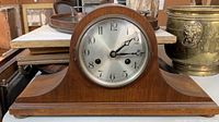 Front view of the antique wooden mantel clock with silver dial, black numerals and hands, sitting on a table with key nearby.