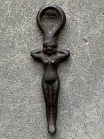 Front view of antique cast iron bottle opener shaped as a nude female figure with hands behind head, showing detailed torso and head loop for bottle opening.