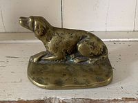 Brass dog figure lying on rectangular base with surface wear and patina