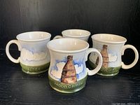 Four ceramic coffee mugs with raised bottle design and 'MOORCROFT' text, set on black surface.