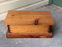 Closed pine box showing dovetail joints and wood grain on top and sides, placed on a gray surface outdoors against a light wall.