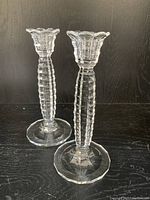 Photo showing a pair of clear glass candlesticks with faceted ribbed stems and octagonal bases on a dark surface against a dark background.
